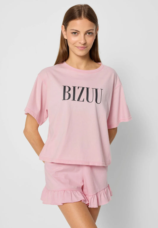 Modelka na tle białej ściany z rękoma z tyłu ubrana w różową piżamę z czarnym logo BIZUU.
