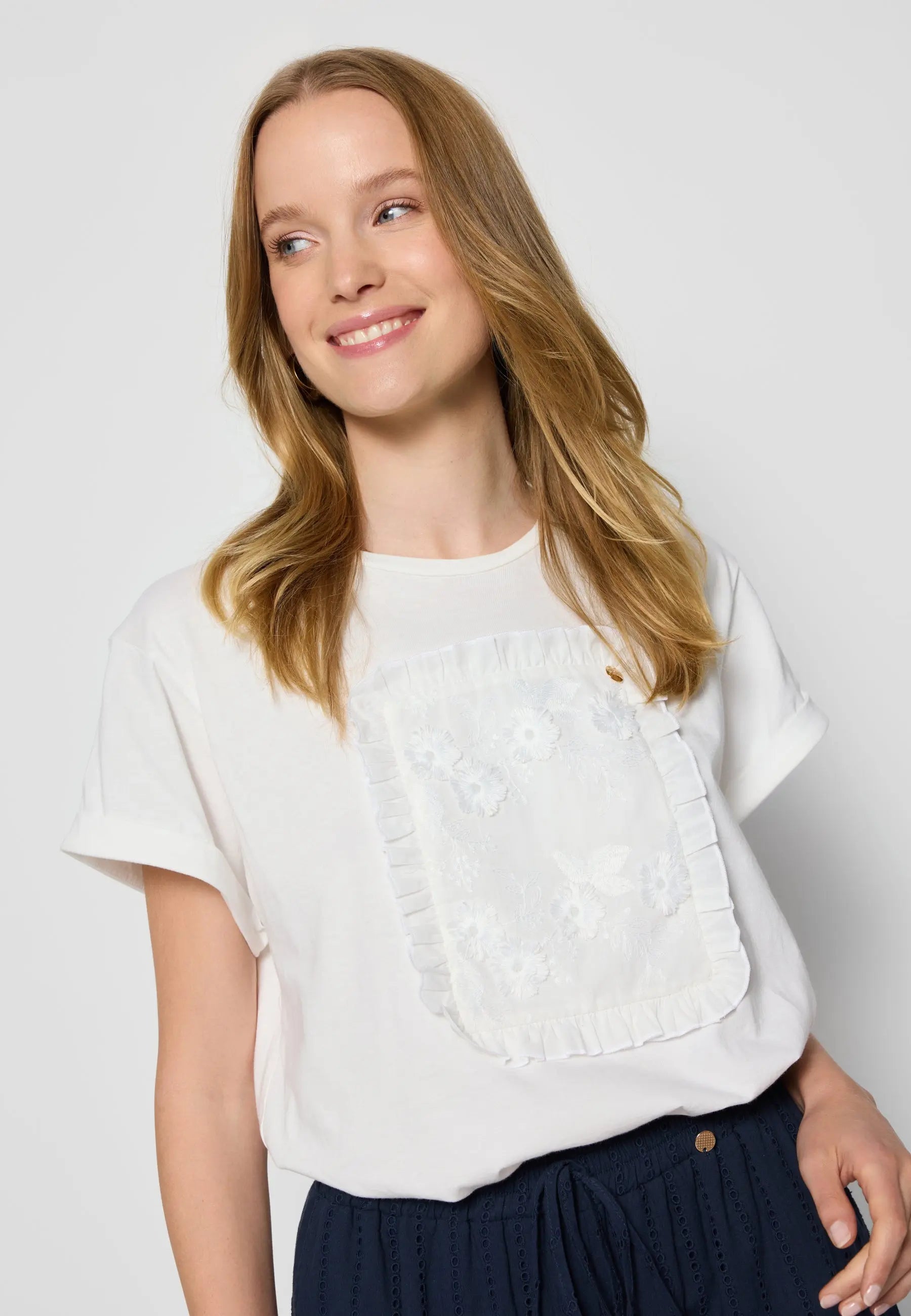 Zbliżenie na kremowy T-shirt z kwiatową aplikacją MIRADO na modelce.