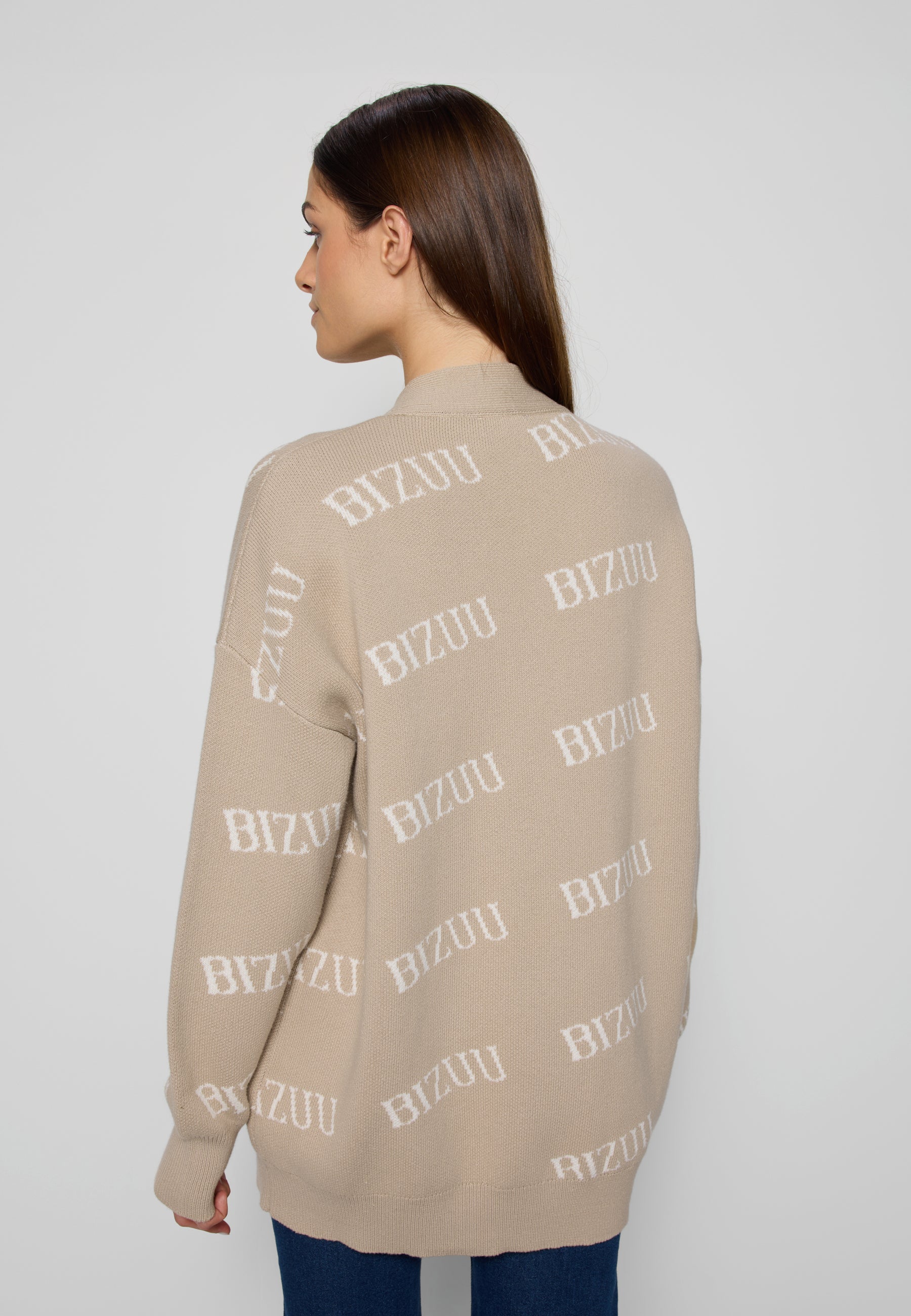 Zbliżenie na modelkę stojącą tyłem na białym tle w beżowym swetrze w logo Kyle.