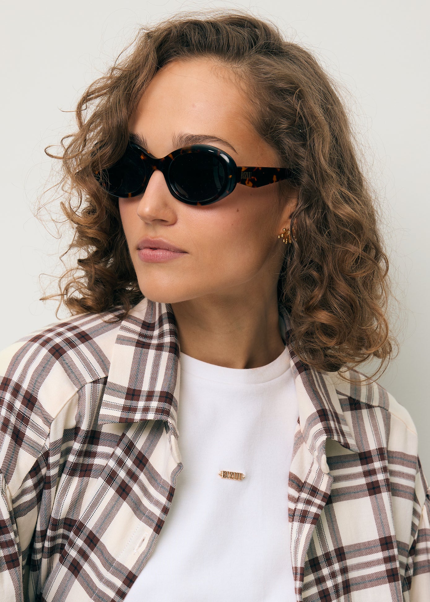 Zbliżenie na modelkę w brązowych okularach ENNA, białym T-shircie TISHALLE oraz w koszuli w kratę FALBI.