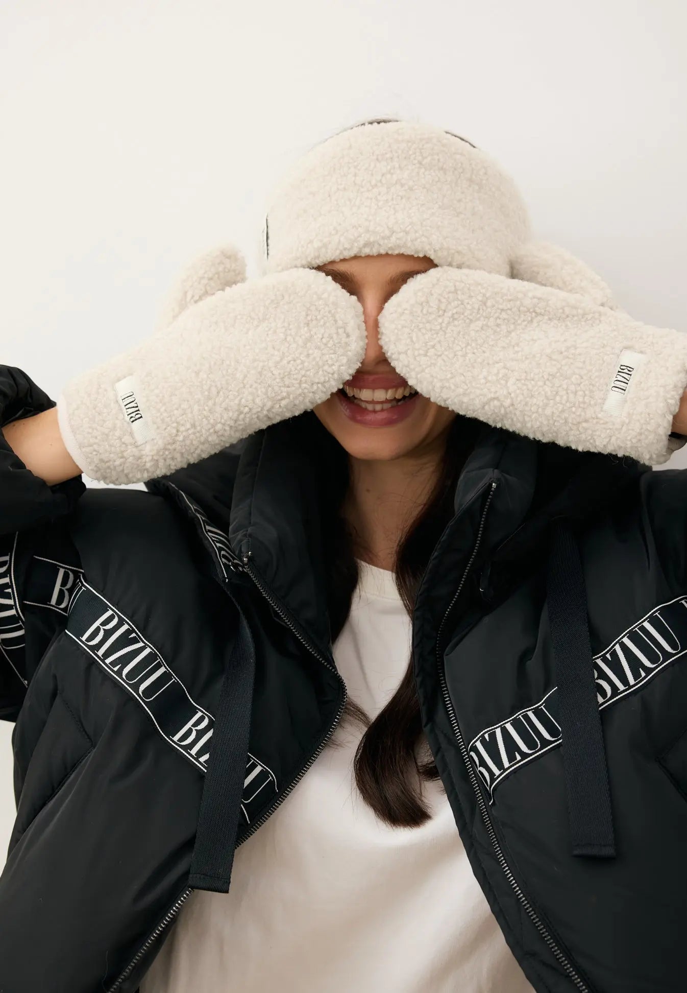 Modelka zasłaniająca oczy kremowymi rękawiczkami SNUGGIE z imitacji kożuszka.