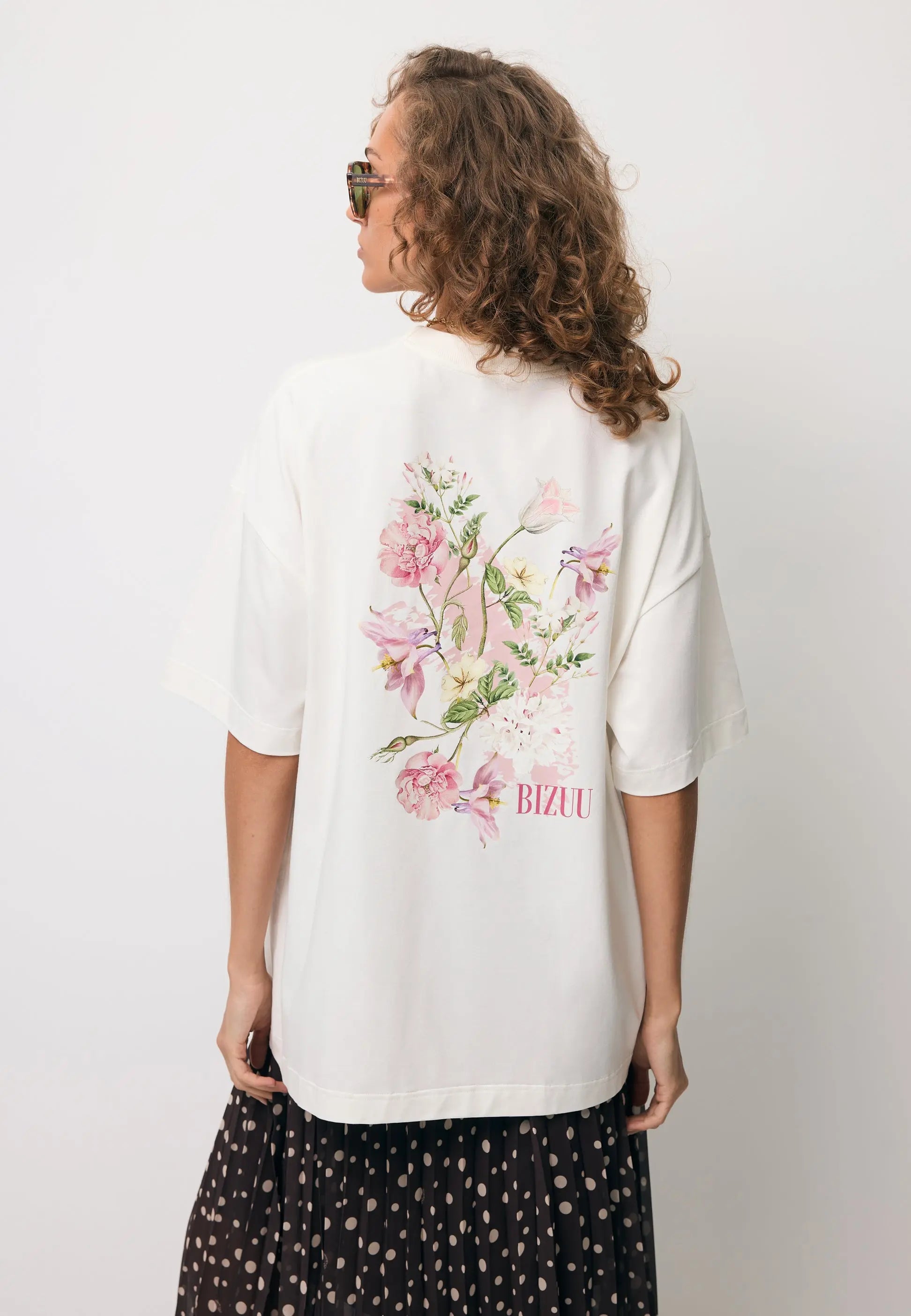 Zbliżenie na modelkę stojącą tyłem w T-shircie RIONA z nadrukiem na tyle.