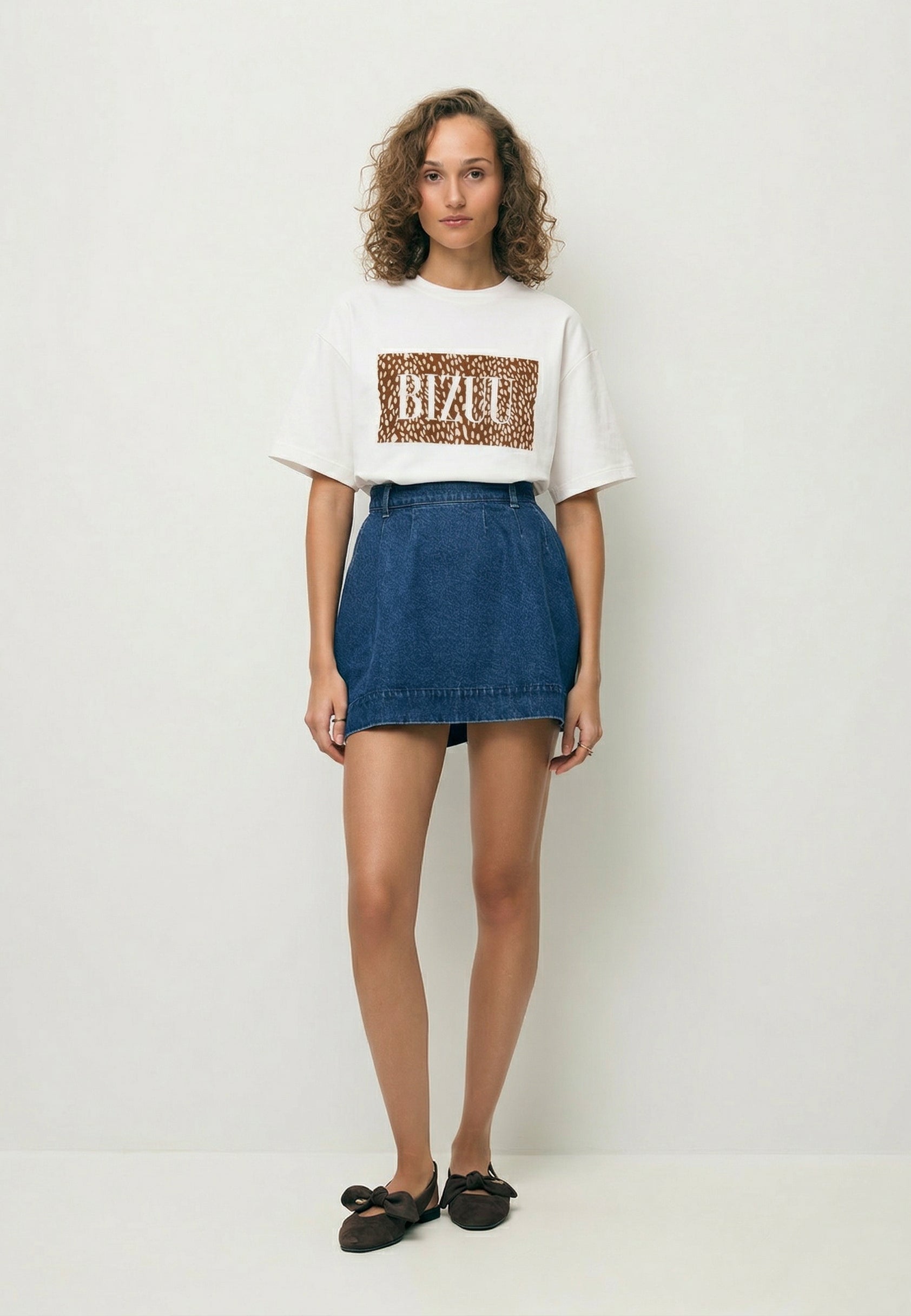 Modelka ubrana w kremową koszulkę SIME z motywem zwierzęcym oraz niebieską spódniczkę z denimu BREDA.