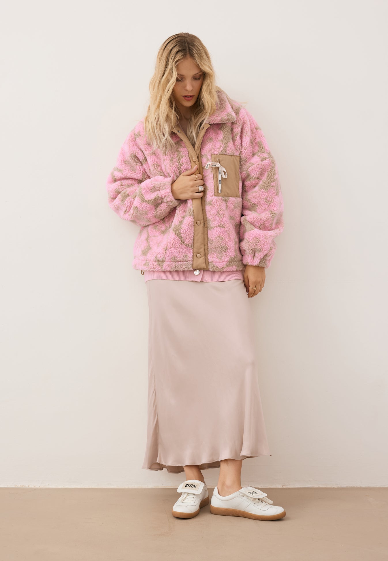 Modelka spoglądająca w dół ubrana w kwiecistą kurtkę z polaru TEDDY, beżową spódnicę BREE oraz sneakersy MOBBY.