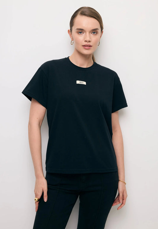 Modelka na tle białej ściany ubrana w klasyczny T-shirt w kolorze czarnym i logo na przodzie TISHALLE.